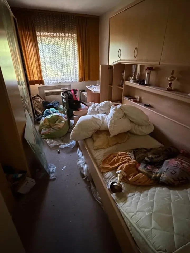 Schlafzimmer vorher: Bett, Schrankwand, Kleidung und Tüten auf dem Boden